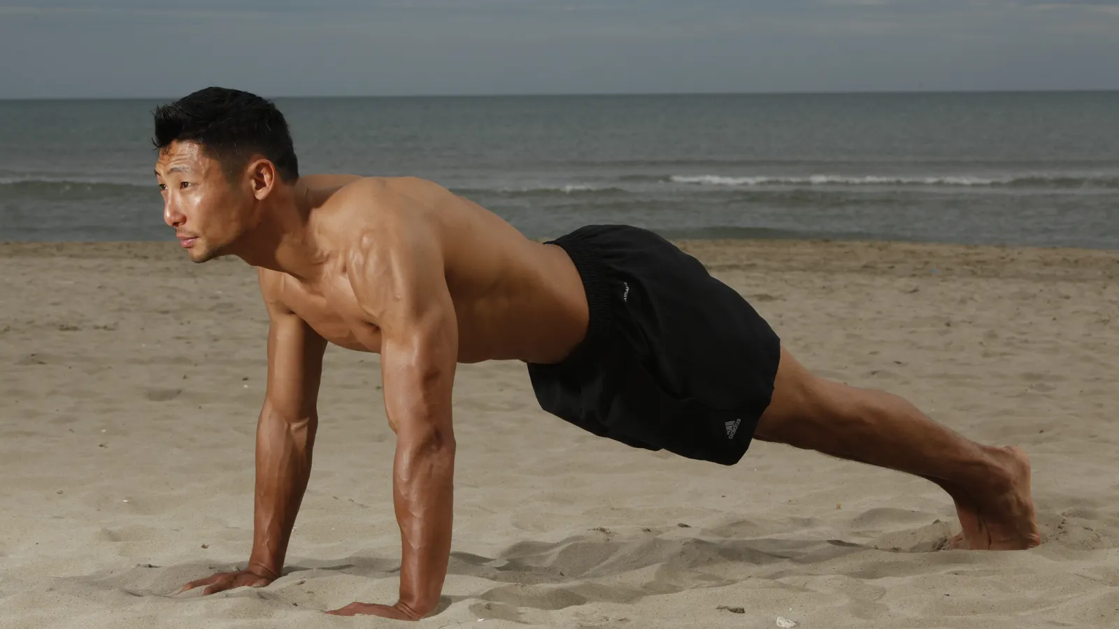 Man holding a plank exercise on the sand at the beach